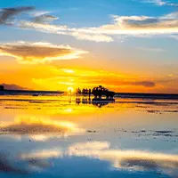 Pôr do sol refletido no Salar de Uyuni, com céu alaranjado e espelho d’água na Bolívia