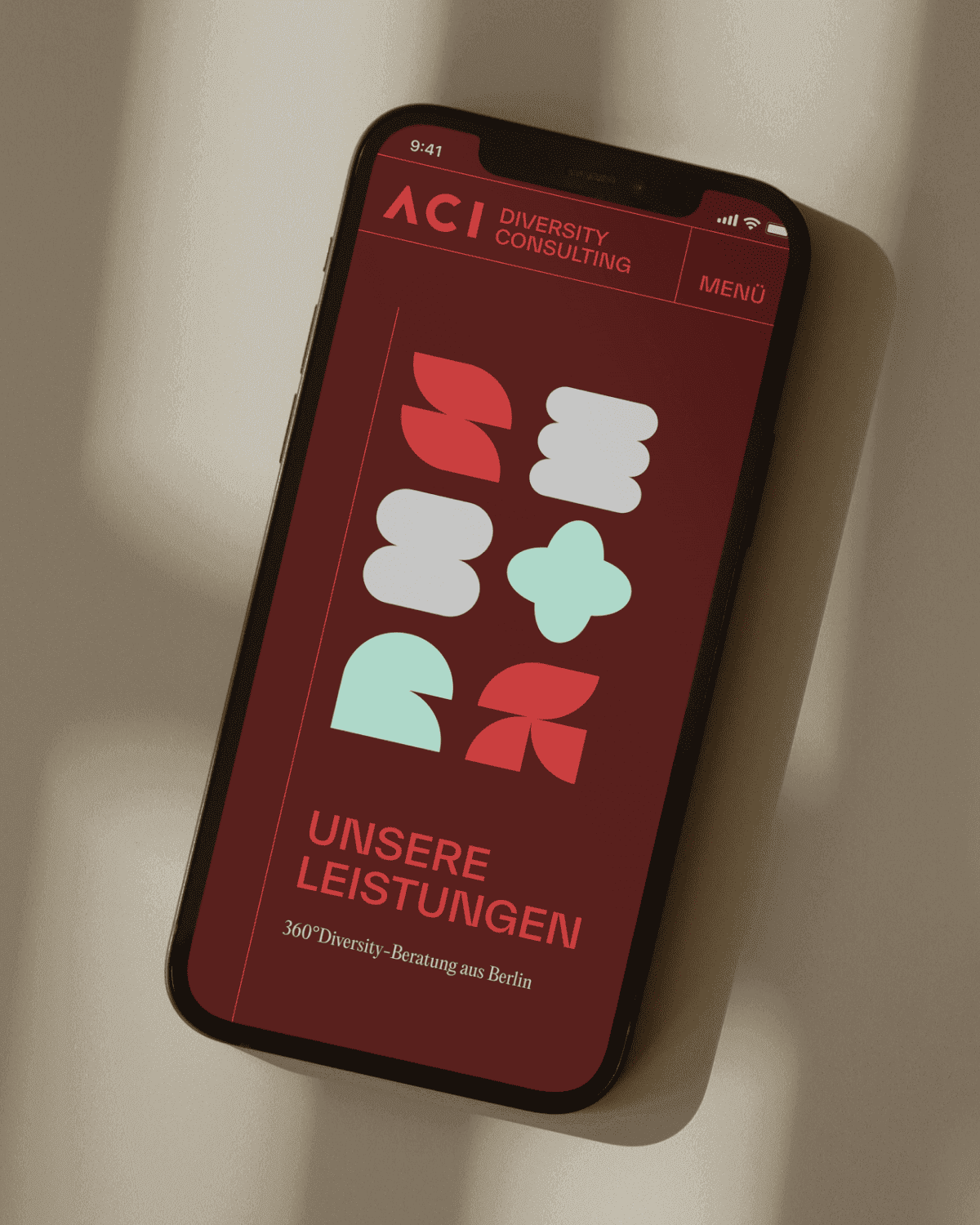 Phone mockup displaying the ACI Consulting website on a dark red background with abstract geometric shapes in mint and white