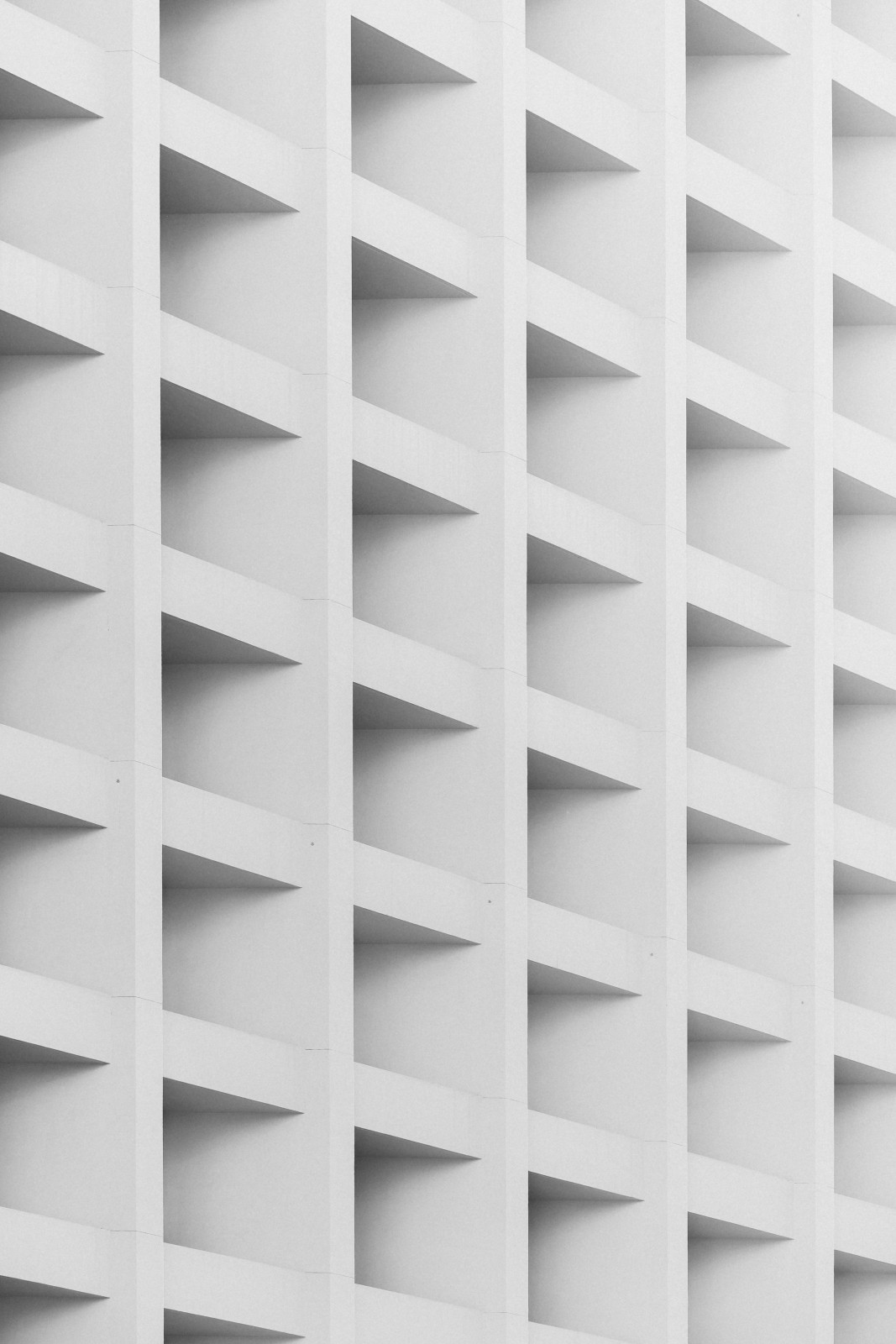 Abstract wall design featuring repeated triangular patterns casting subtle shadows. Monochromatic gray tones dominate.