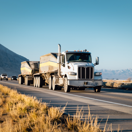 White semi-truck with trailer driving on a mountain highway during daylight.