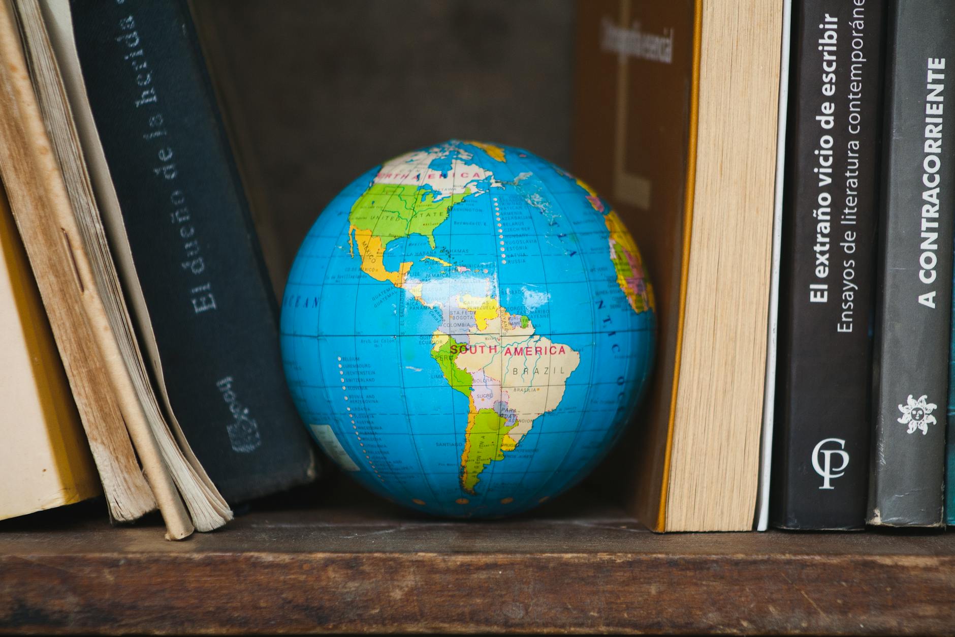 An antique world map and brass compass resting on a wooden desk next to a stack of historical biographies.