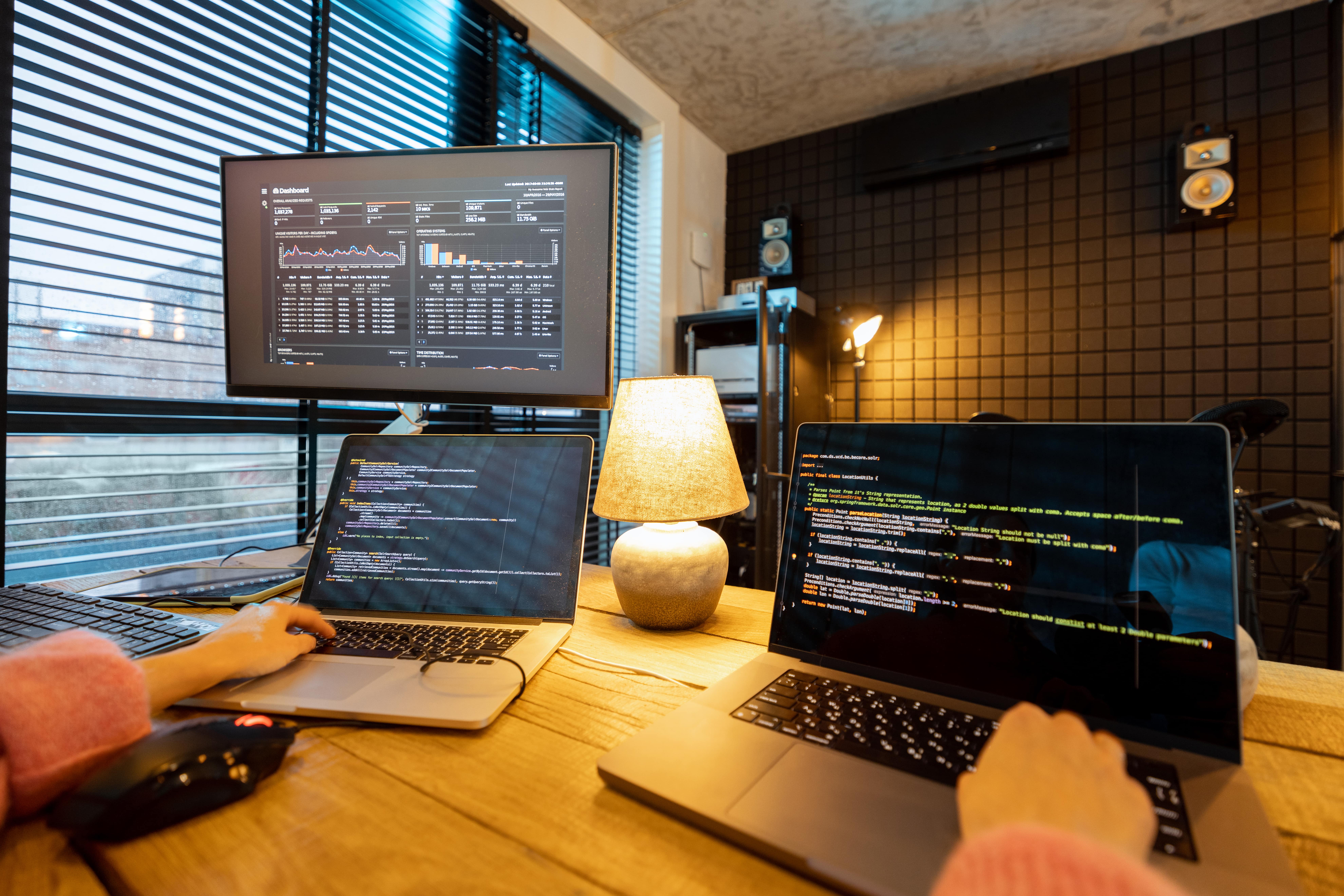 Female programmers coding at a shared workspace with data analytics dashboard on screen.