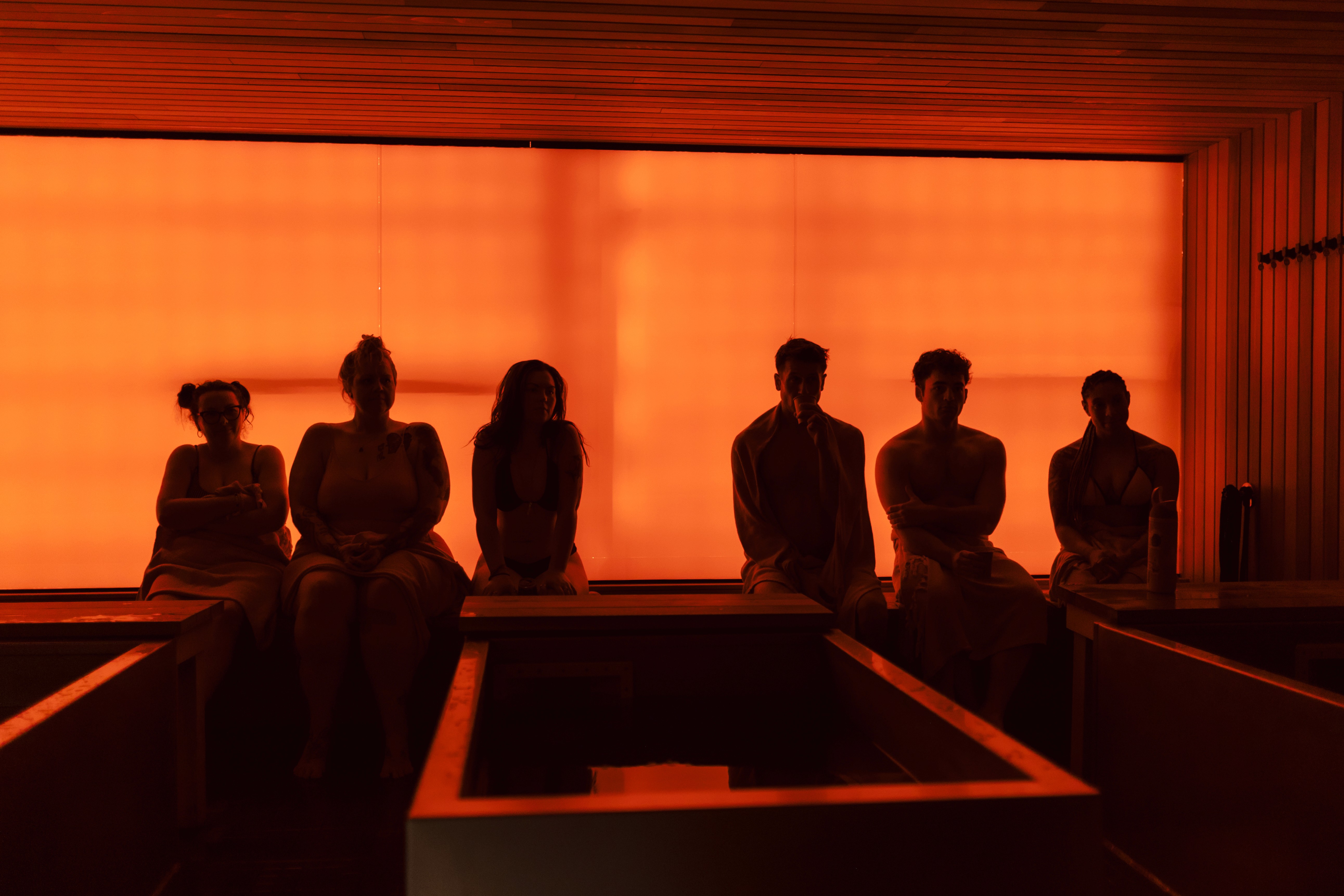 Four friends laughing together outdoors in natural light, dressed in neutral casual outfits.