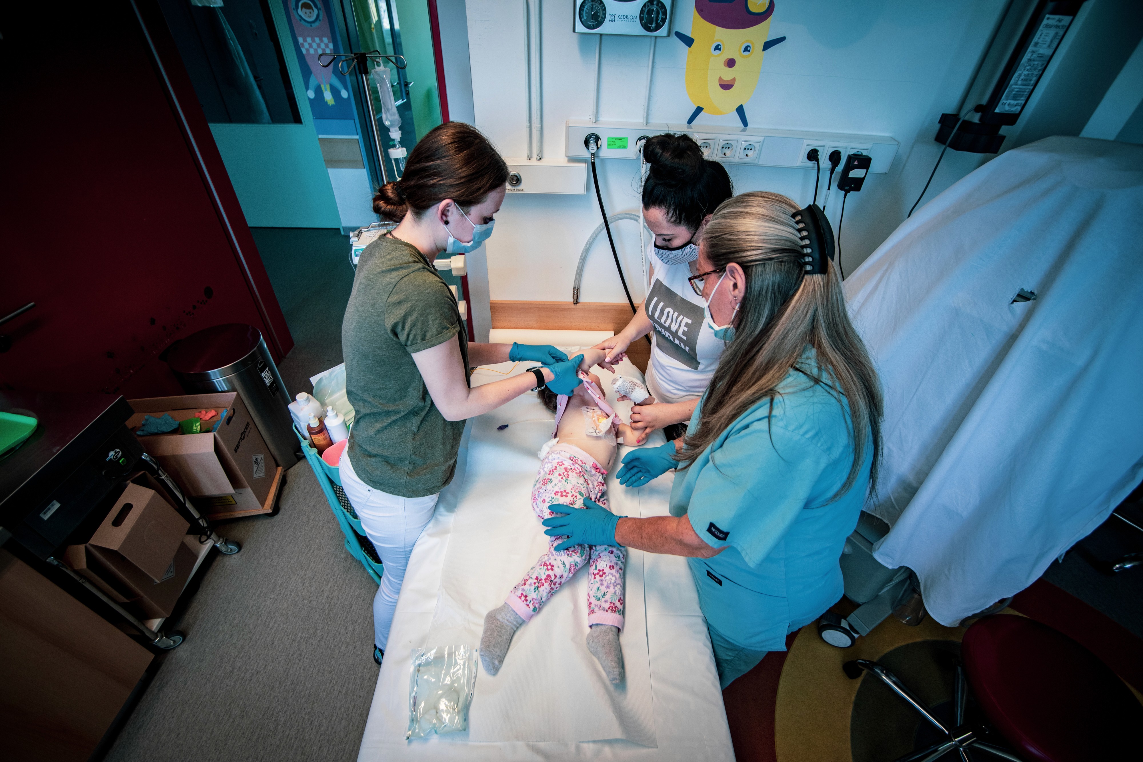 Három egészségügyi dolgozó lát el egy kislányt orvosi ágyon.