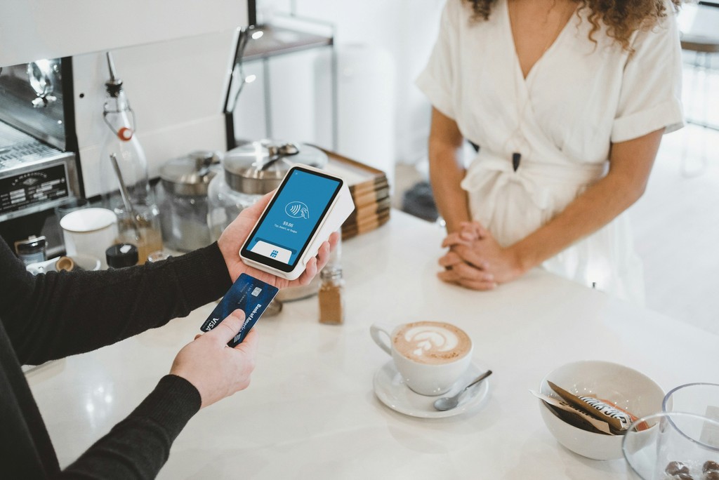 A man is holding a credit card while standing in front of a coffee table, showcasing a casual shopping moment.