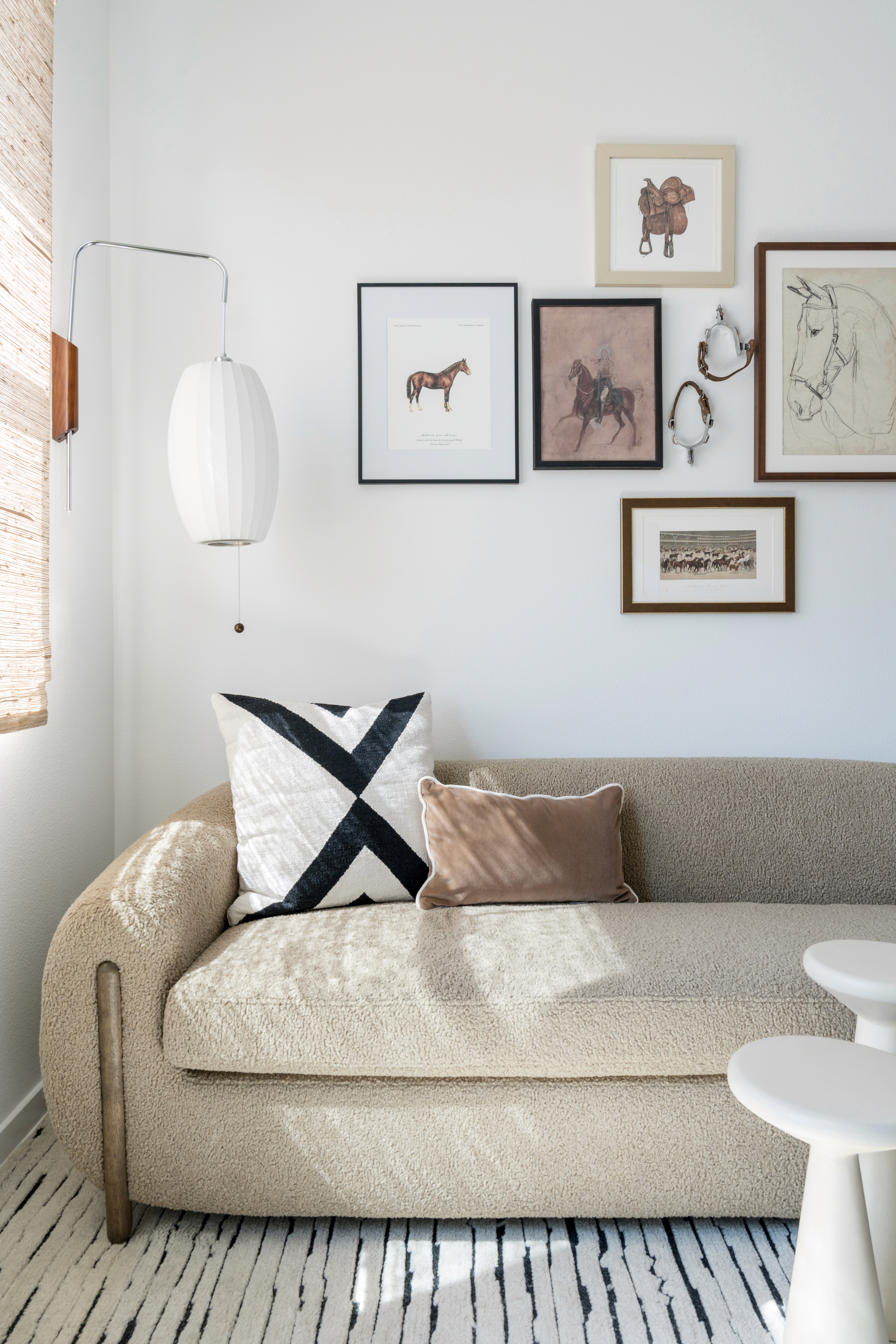 Bright seating area with boucle love seat, white, black and brown pillows, tiered accent tables, white and black textured area rug, and western gallery wall by Jubilee Interiors in Arcadia, California