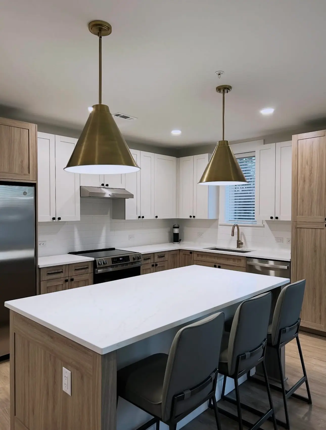Pristine Airbnb kitchen after turnover cleaning featuring a sparkling white island, polished gold pendant lights, and sanitized wood cabinetry.