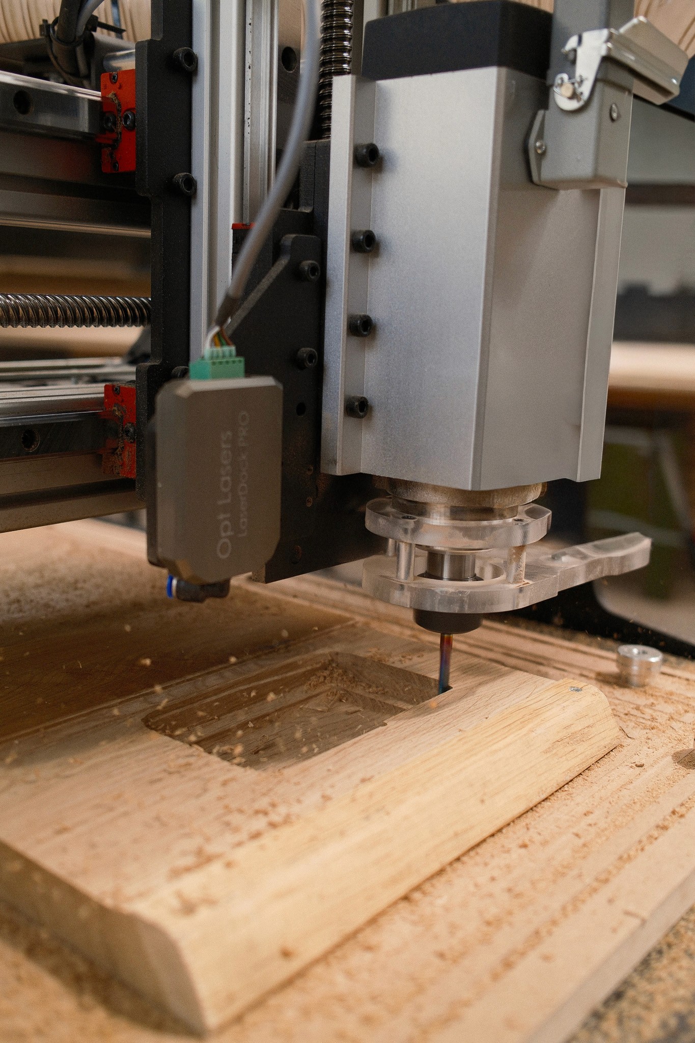CNC-Fräse bearbeitet ein Holzbrett, im Hintergrund das Lasermodul am Schlitten