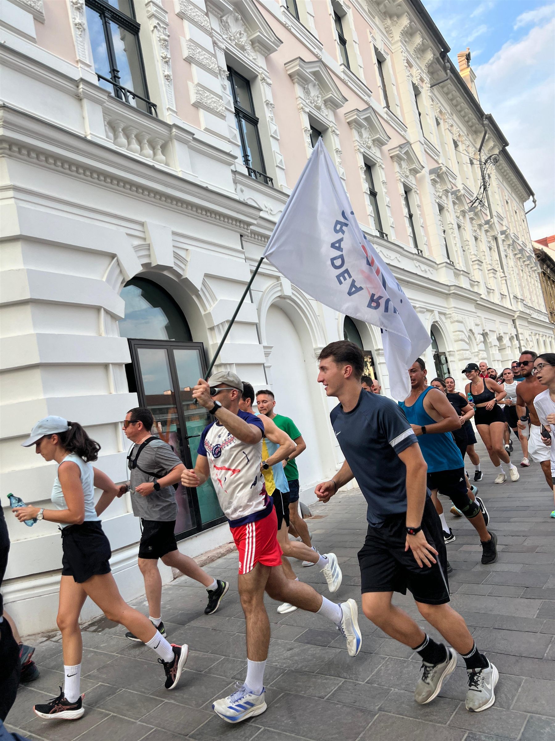 Grupul de alergători ORC parcurge centrul orașului cu steagul comunității.