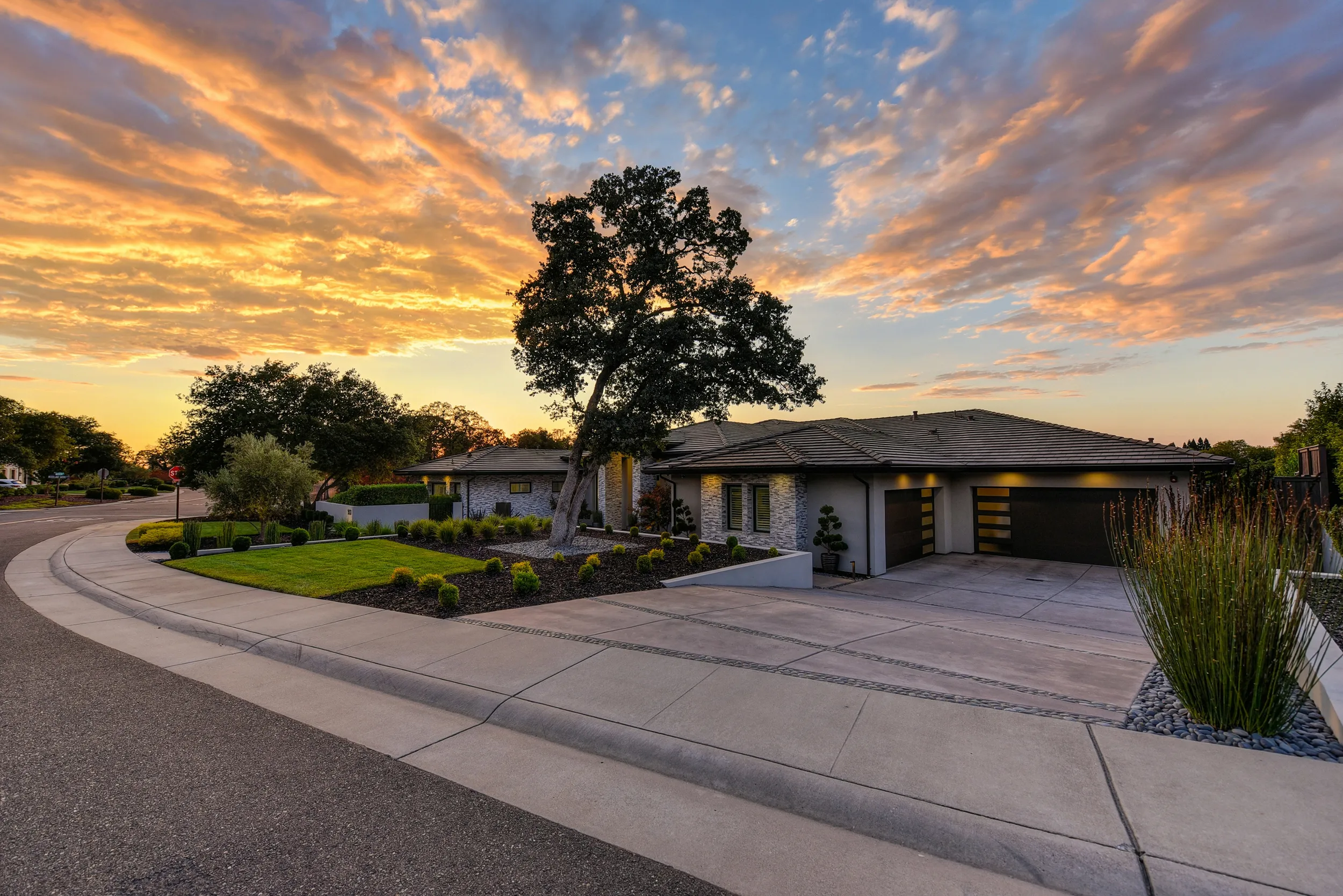 Single-story suburban house at sunset, landscaped front yard and curved driveway