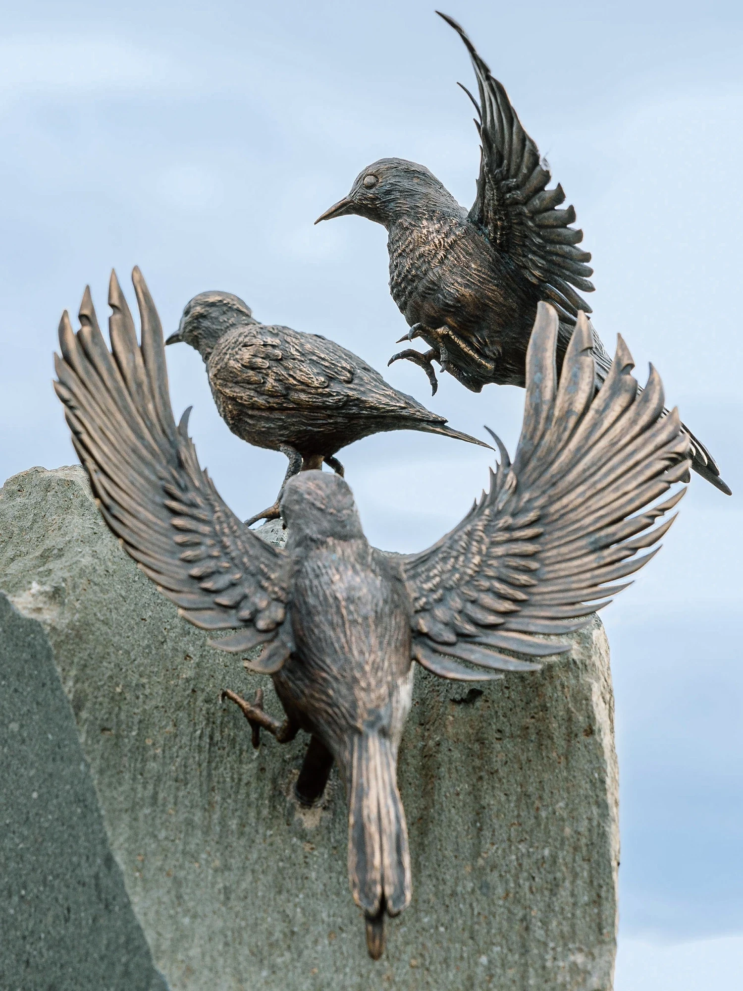 Close-up of sculpted bronze birds taking flight atop a custom slate stone monument created by artist Shaun Leane.