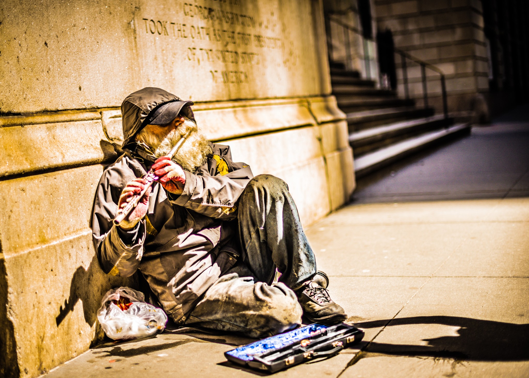 A homelss man playing the flute outside of the exchange on Wall Street