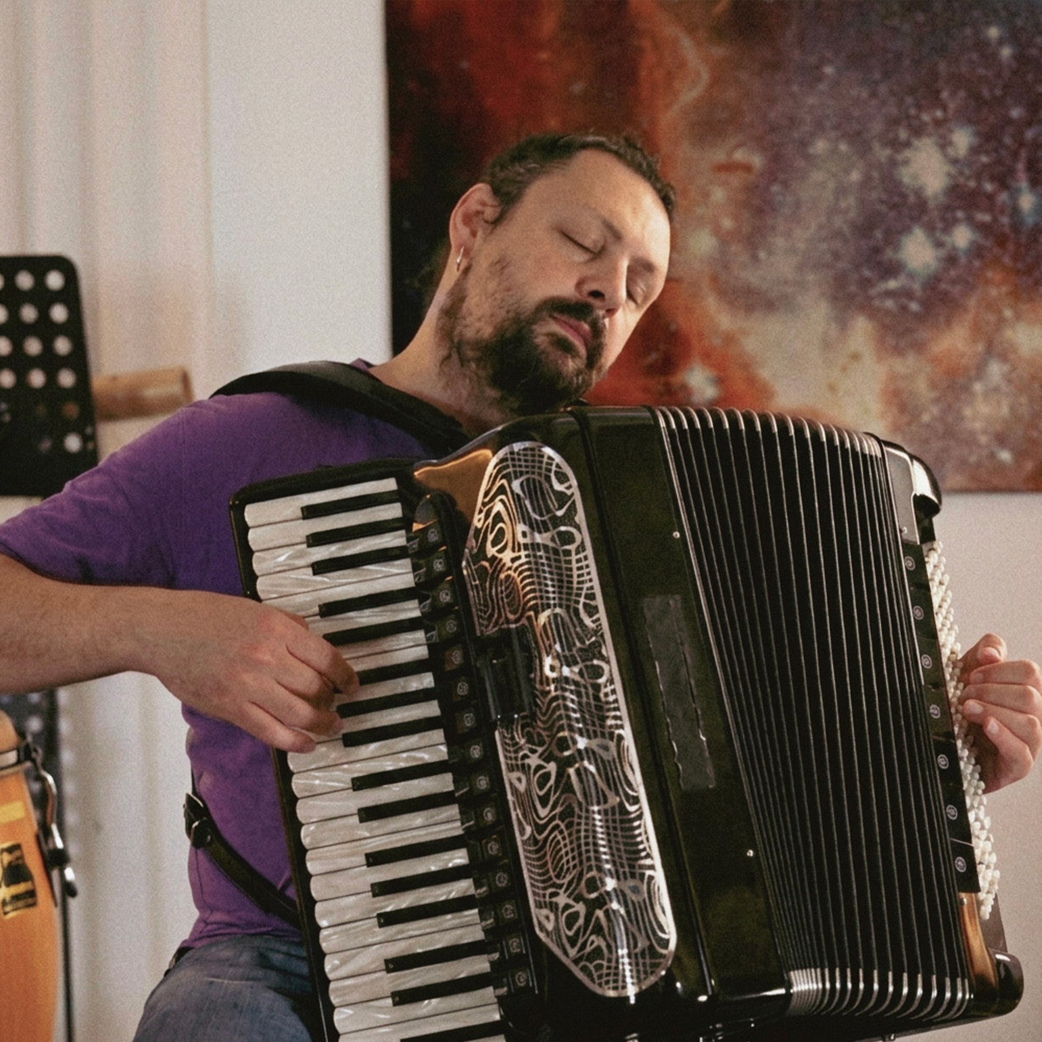 Mor tişörtüyle gözleri kapalı bir şekilde siyah akordeonunu çalan müzisyen Mikordeon.