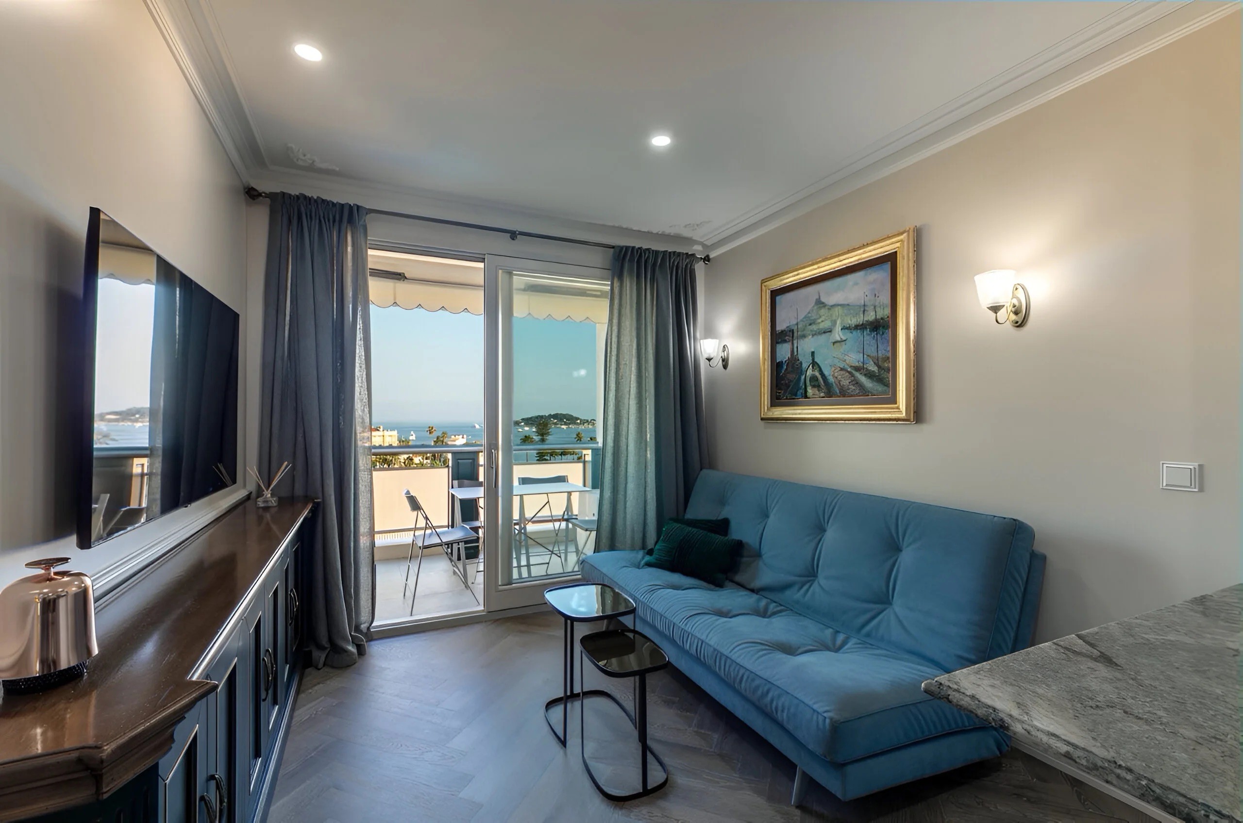 Aperçu du projet Beaulieu : Salon de standing avec canapé bleu profond et vue sur la mer depuis le balcon.