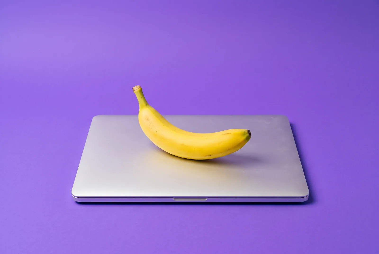 A banana resting on the lid of a closed silver laptop, a playful image for how to block porn on a Mac