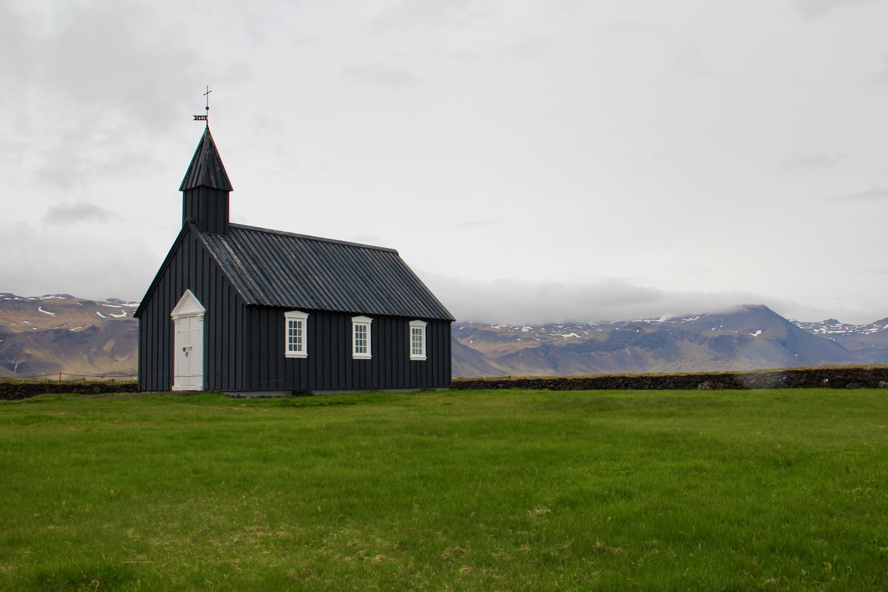 The Black Church of Búðakirkja, a small black chapel, on a green grassy field against a gray sky.