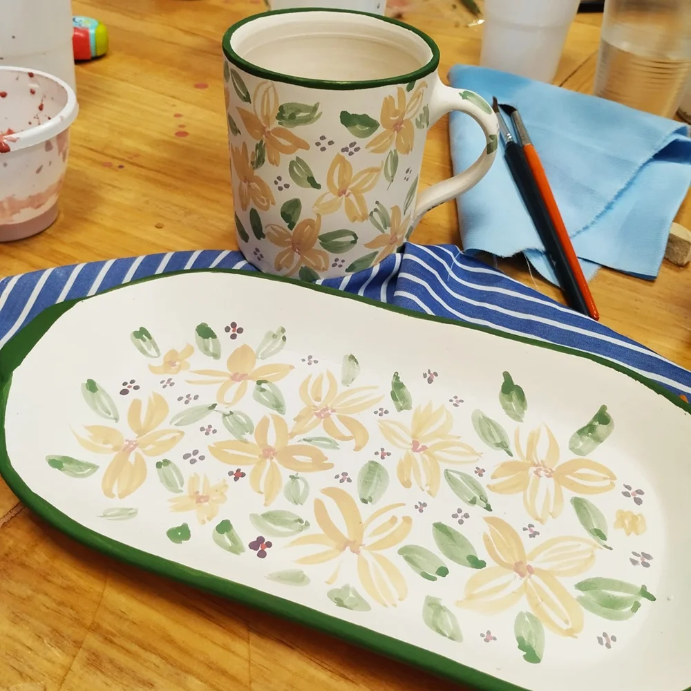 Piezas de vajilla cerámica pintadas a mano con motivos florales durante el proceso de creación.