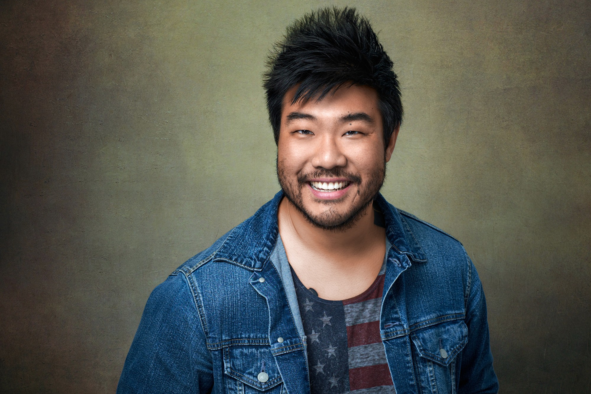 Casual headshot of Asian man in denim shirt smiling at camera