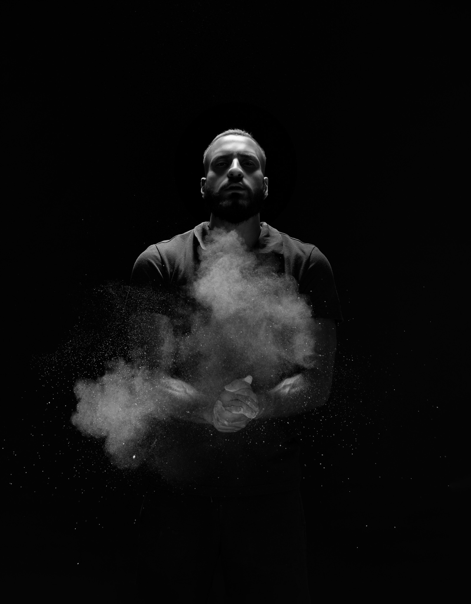 A studio concept shot: a man clapping his chalk-covered hands together in a dark space, sending up a burst of white powder.
