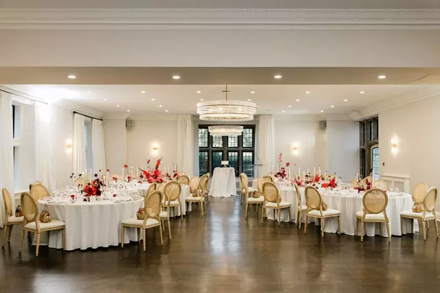 A serene outdoor wedding setup with white chairs arranged on green grass under a canopy of trees.