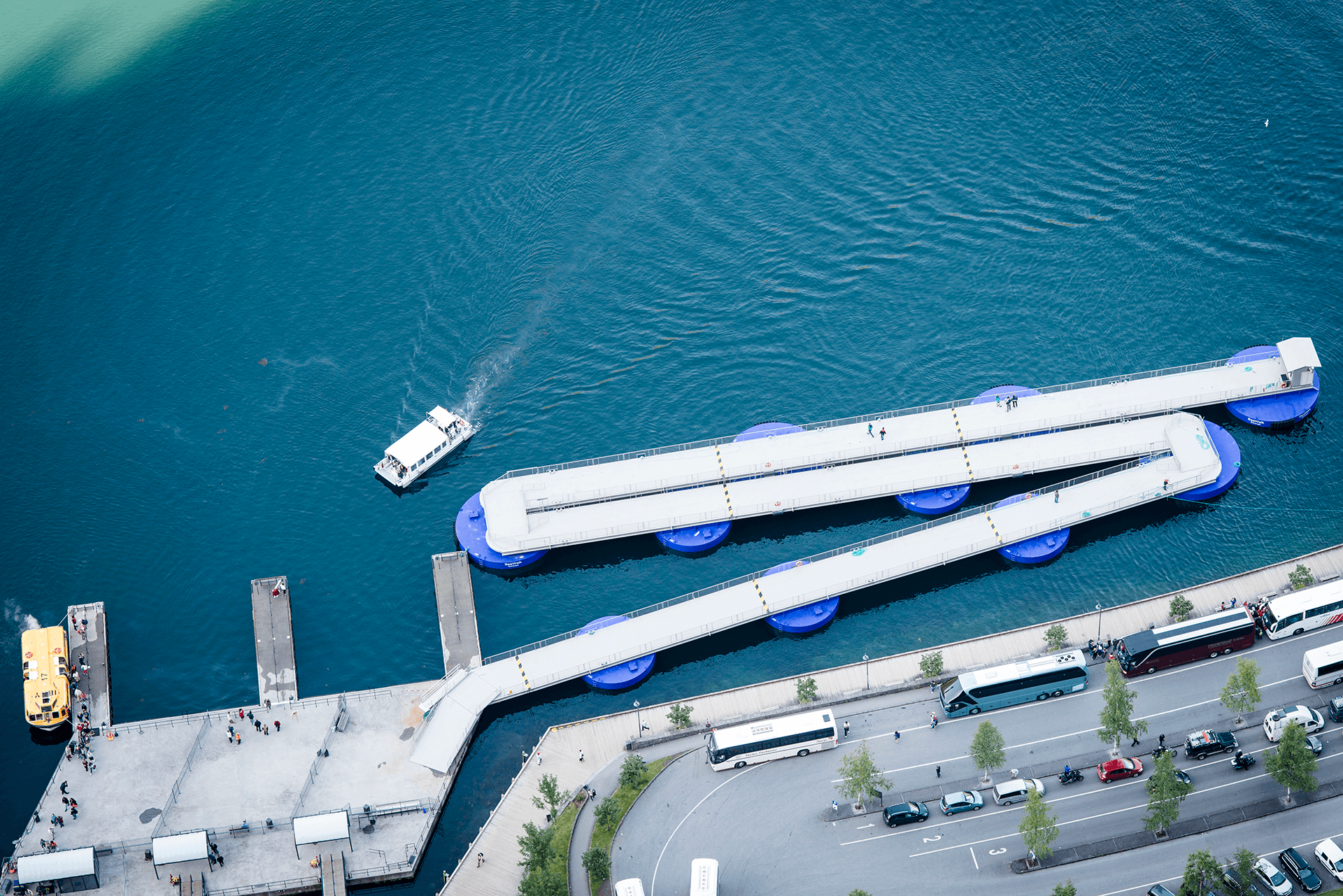 Floating SeaWalk pier system with blue pontoons extending from a quay, connecting shore facilities to open water for cruise and passenger operations.