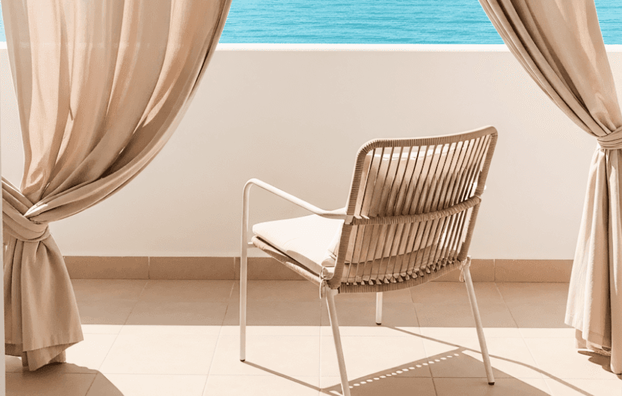Minimalist balcony chair framed by flowing curtains with a serene ocean view.
