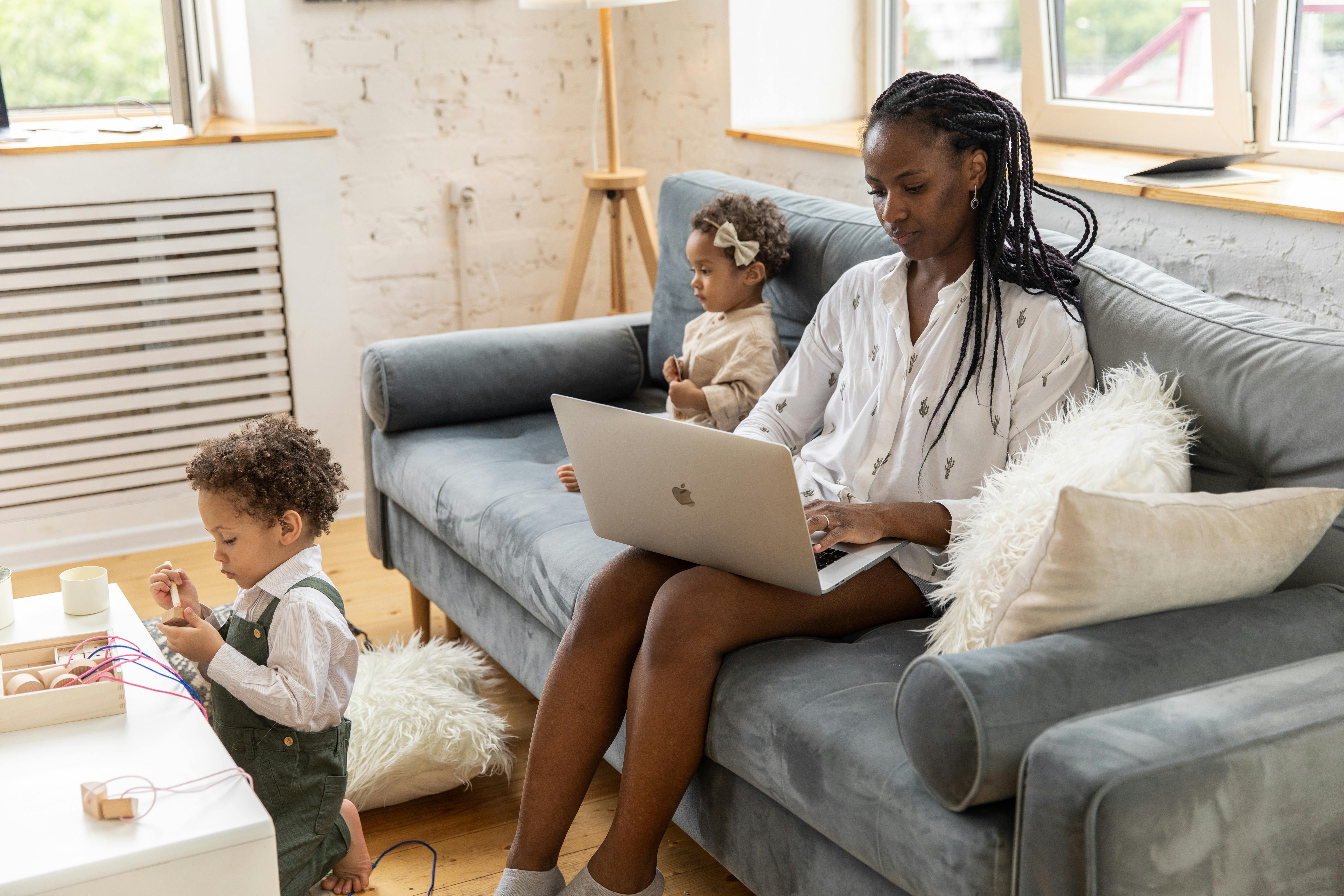 A black woman working from home on a sofa with her two children