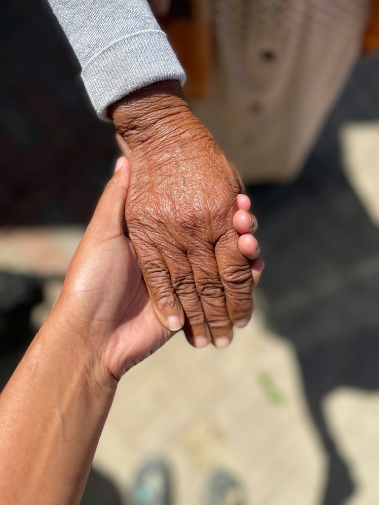 A close-up of a younger person gently holding the hand of an elderly individual, highlighting the contrast between the smooth and wrinkled skin, symbolizing care and connection across generations.