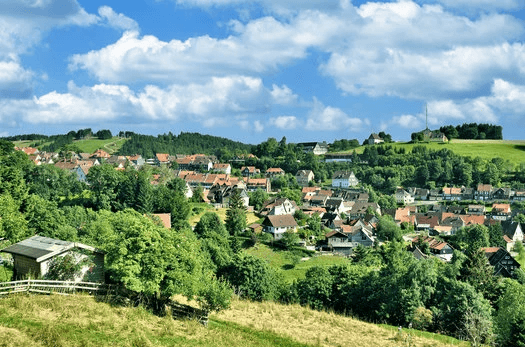 A wooden desk by a window, with sunlight illuminating a laptop, notebook, and a decorative vase.