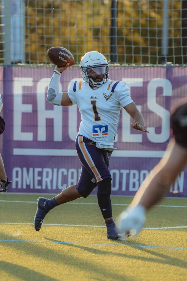 Der Quarterback der Bucks in Weiß läuft mit dem Ball in der Hand vor einer Bande mit Eagles-Schriftzug.