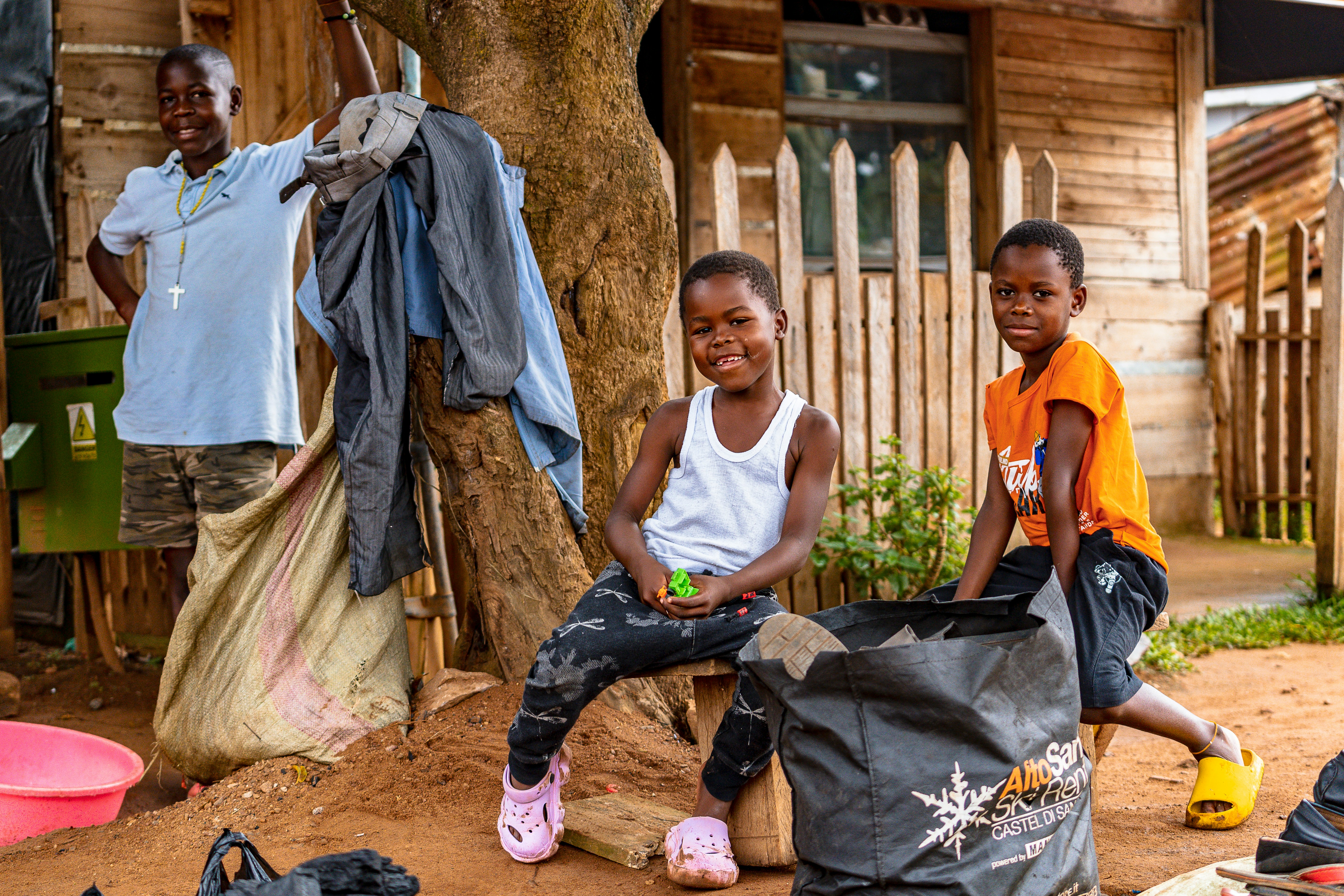 Two smiling children in front of a wooden house.