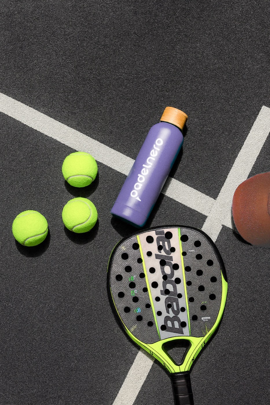 Essentials des Spiels – Schläger, Bälle und die Padelnero-Flasche auf dem ikonischen schwarzen Court.