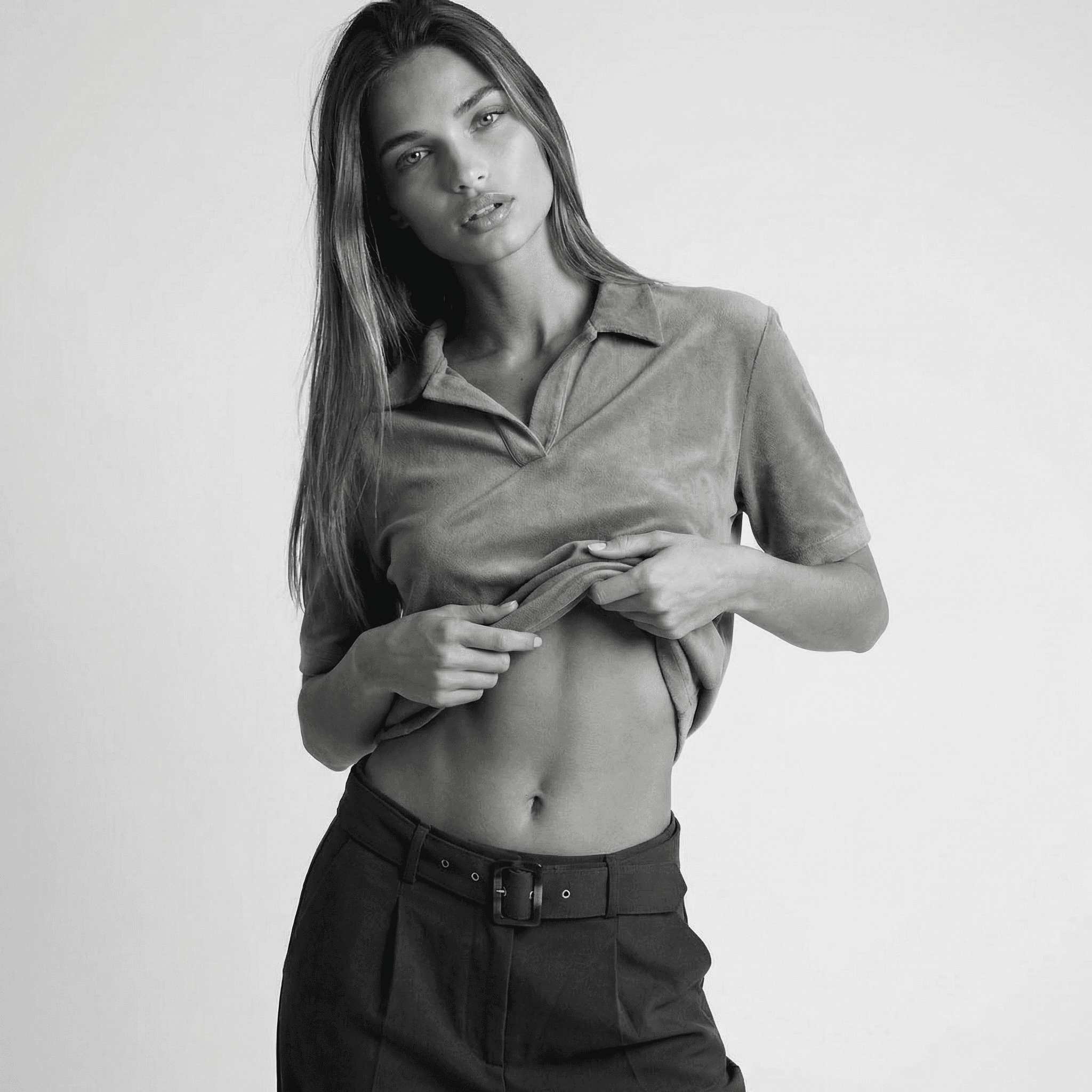 KI-Model in schwarzem Top und Bikini am sonnigen Strand, natürliche Pose mit erhobenem Arm, weiches Abendlicht und ruhige Meereskulisse