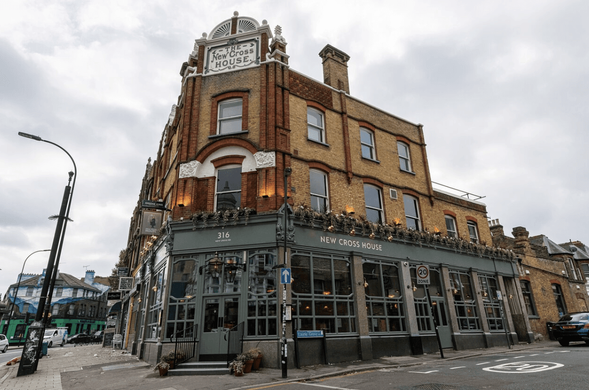 A smiling man with curly hair is sitting at a desk, looking at the camera, with a laptop and a lamp in the background.
