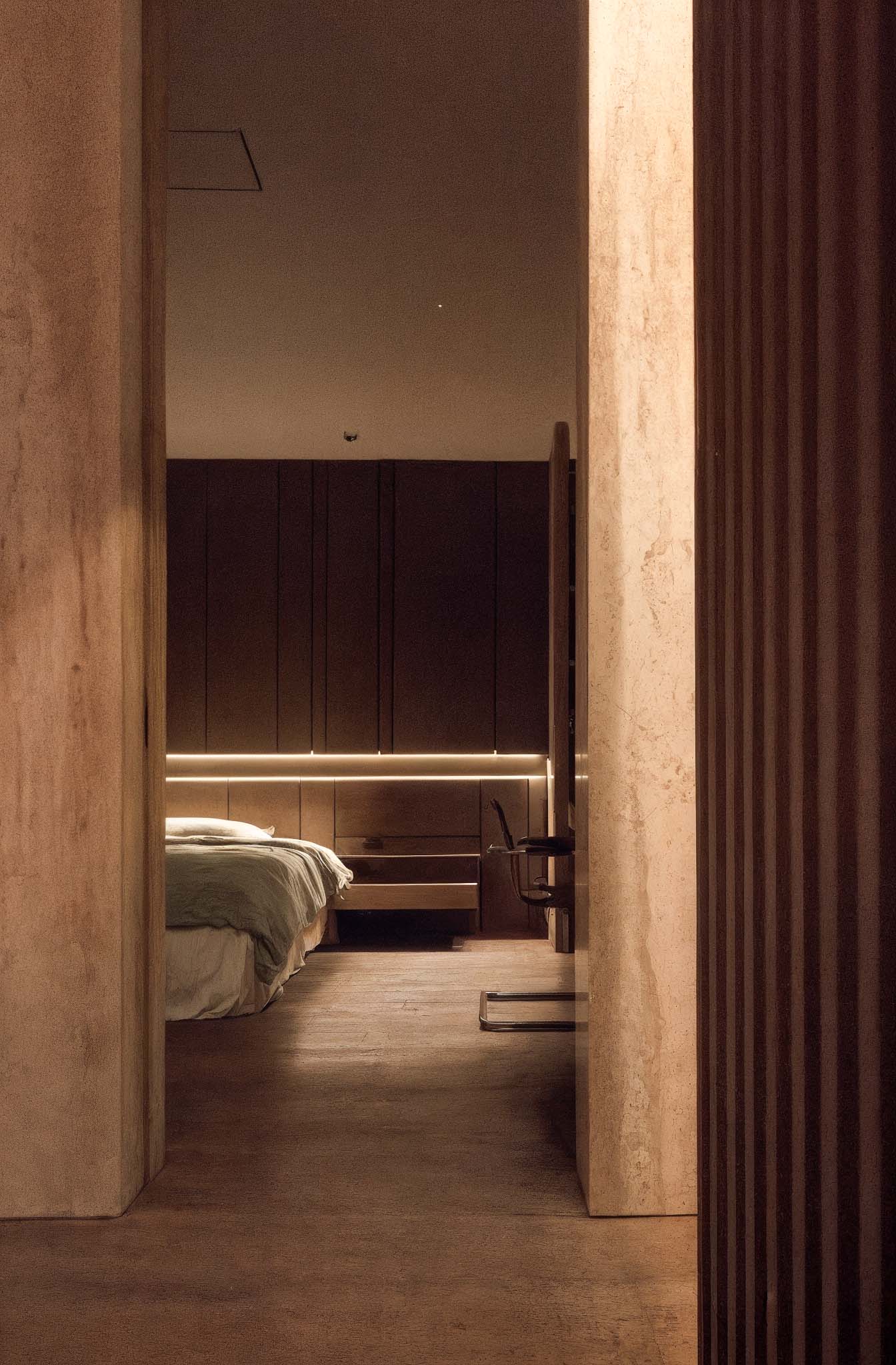 夜間臥房透過間接照明勾勒床頭與木作櫃體線條，整體色調溫潤沉穩