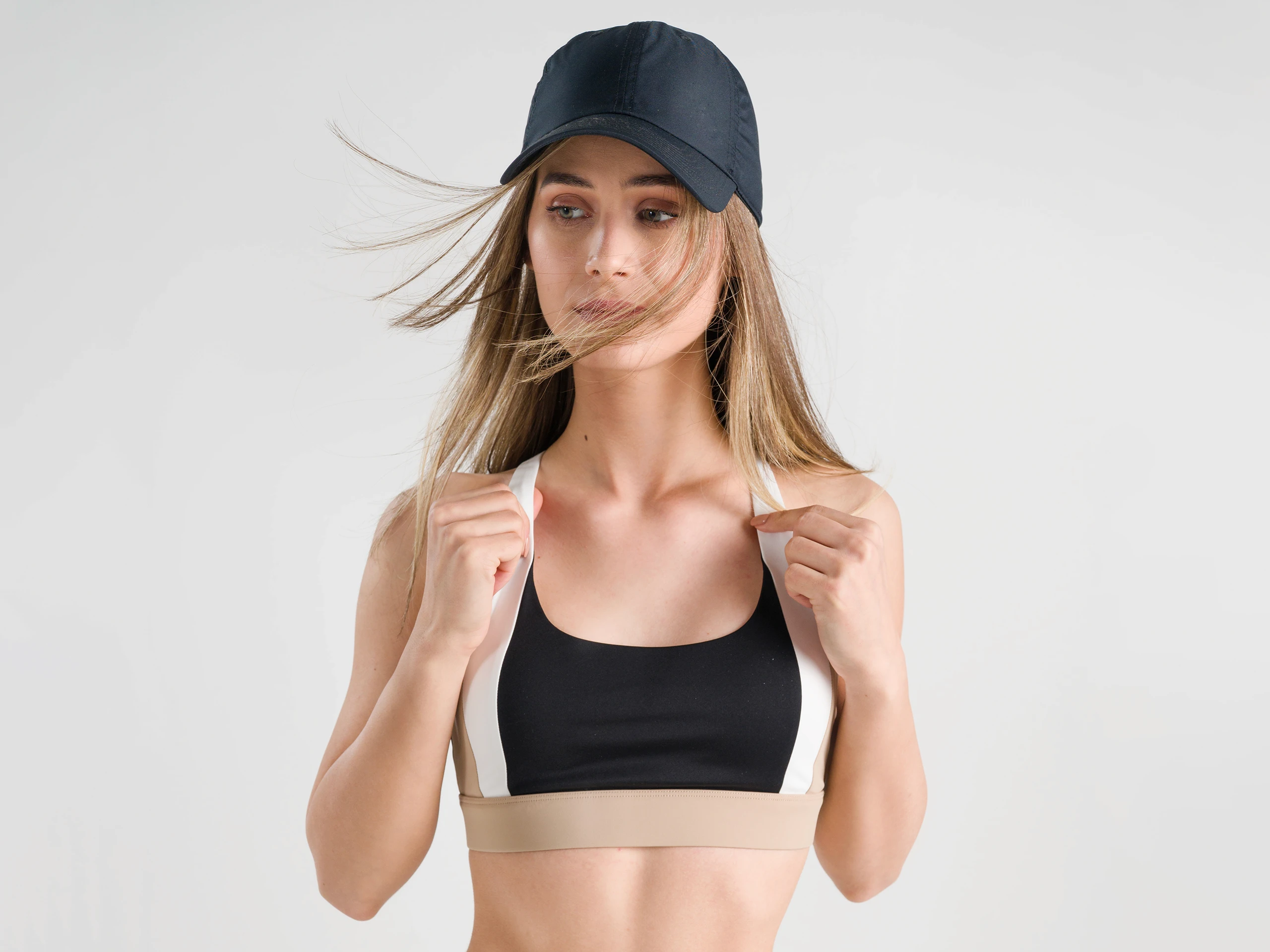 Female athlete in beige cycling shorts and a black sports bra, posing in a studio.