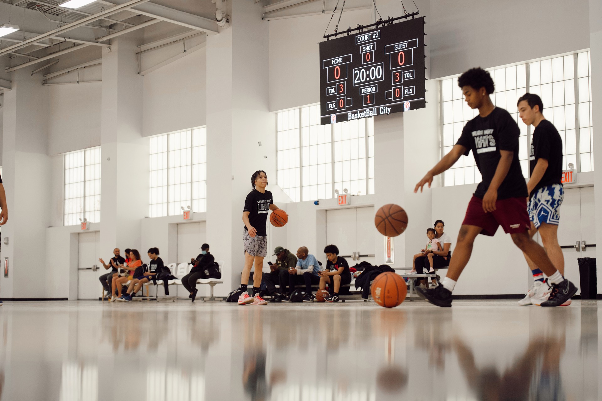 Group of young athletes dribble basketballs inside of a gym.