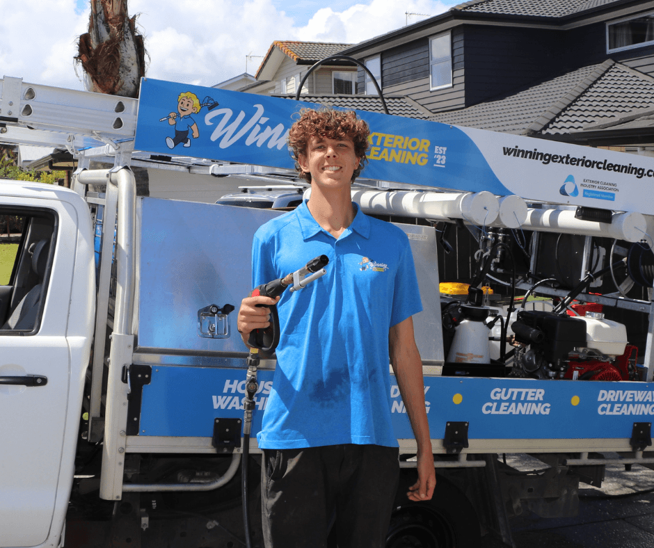 Asher standing in front of Winning Window Cleaning truck with house washing setup on display