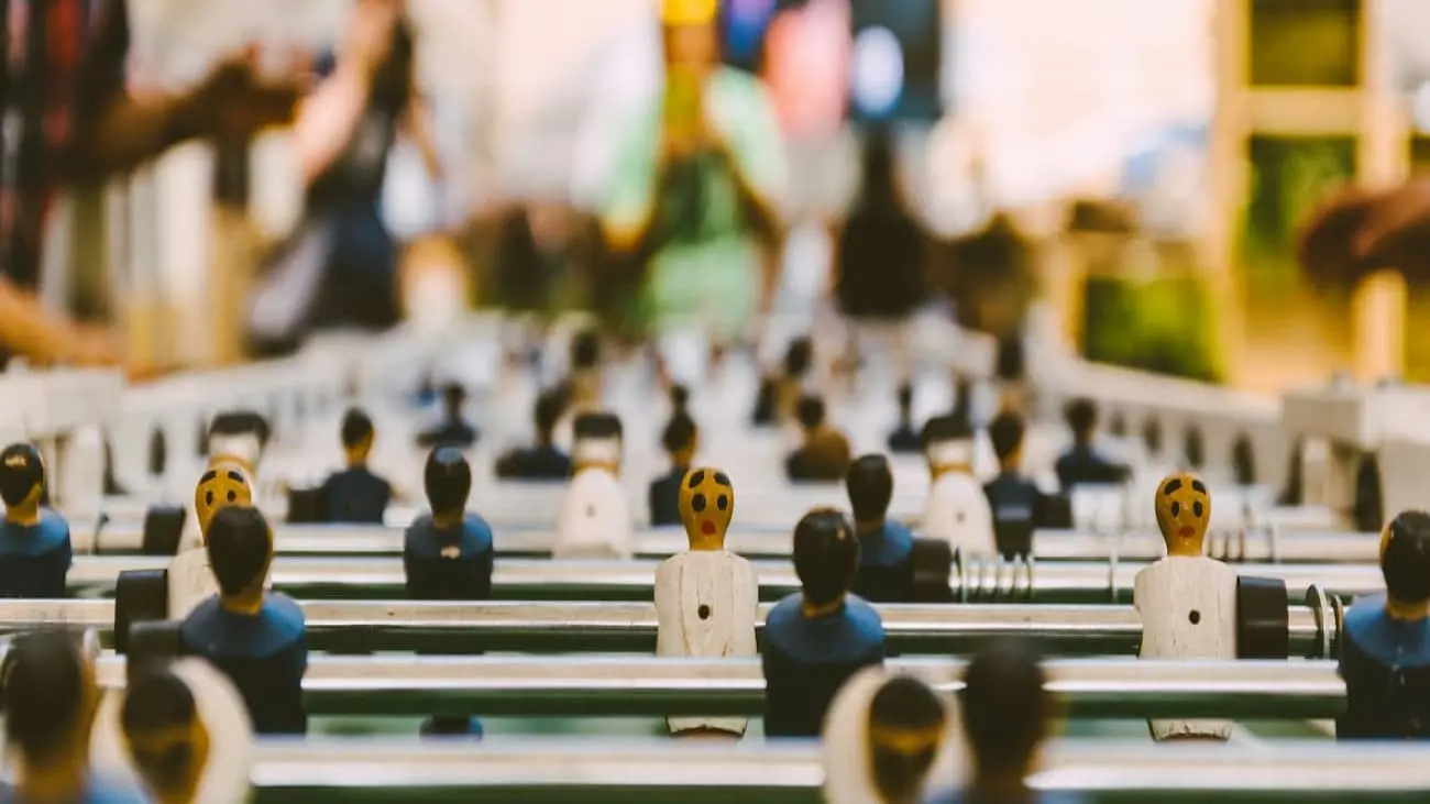 Close-up view of a foosball table with several player figures in focus, set against a blurred background. The image captures the intensity and fun of foosball tournaments, making it ideal for discussing CoachingArea's tools for organising table football events. The foosball players are in blue and white jerseys, representing teams on opposite sides of the game.