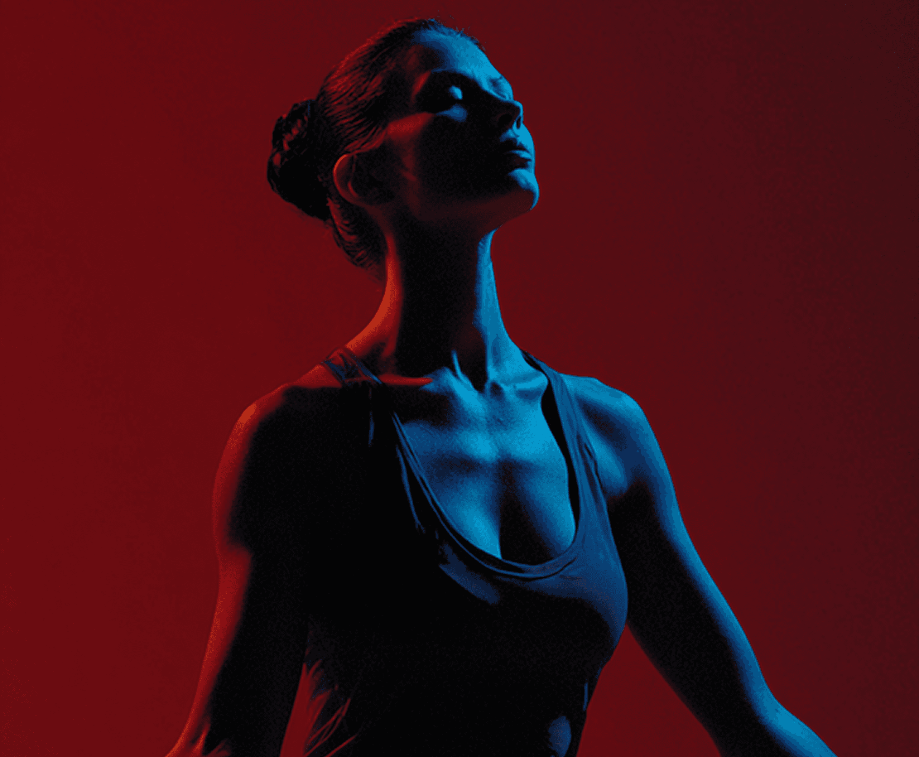 Woman in dark top, bathed in red and blue light, looking upward.