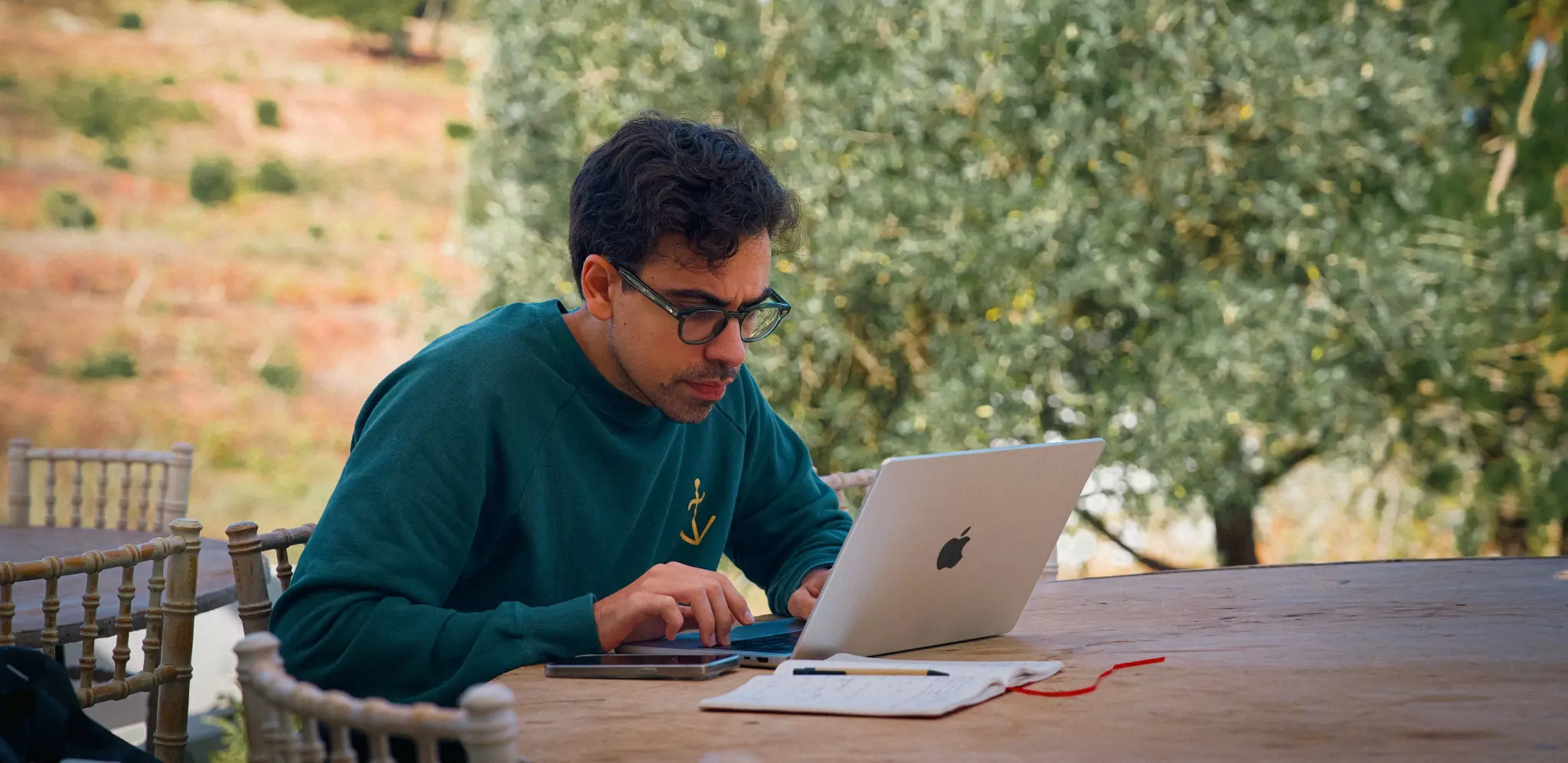 Man in glasses working on laptop outdoors.