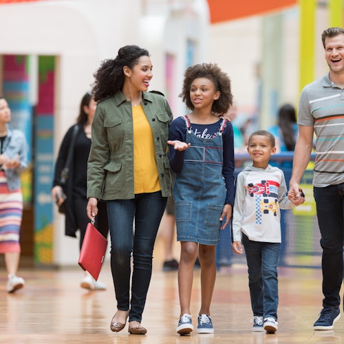 一家四口，包括兩個成年人和兩個小孩，走進一家明亮的購物中心，笑著聊天。