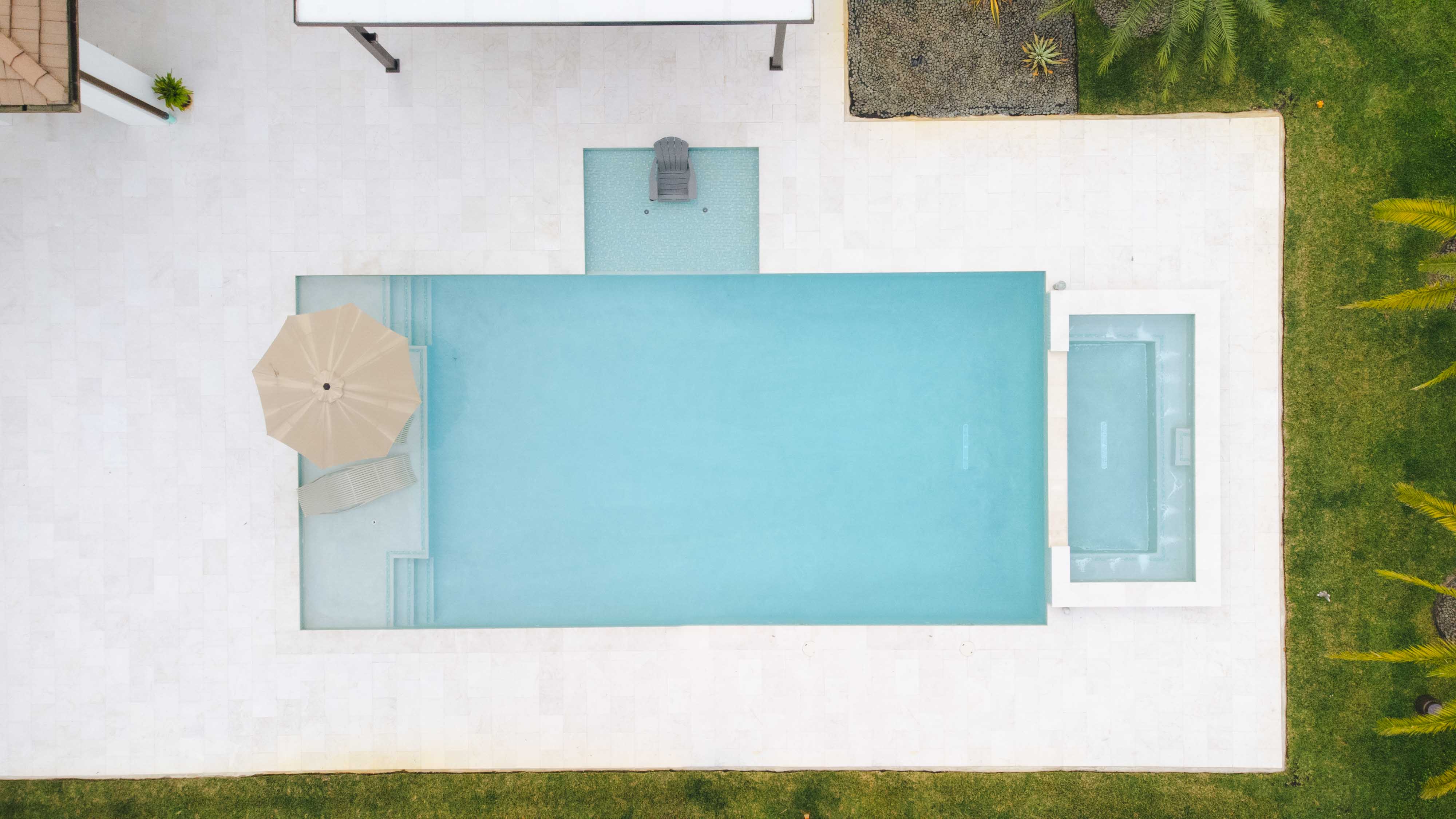 Aerial view of a modern infinity pool and hot tub with umbrella and lounge chair.