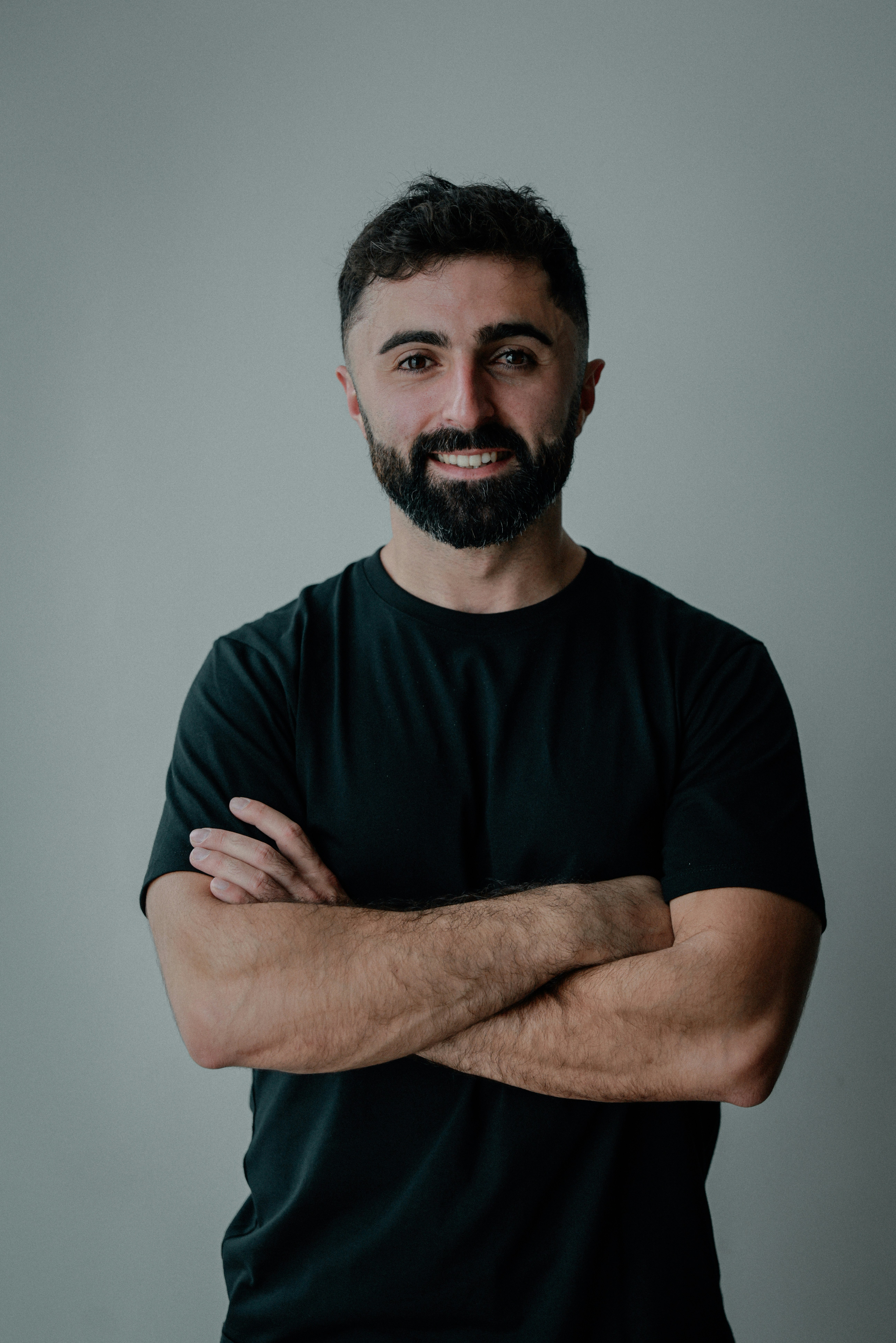 A man with a beard smiles with arms crossed.