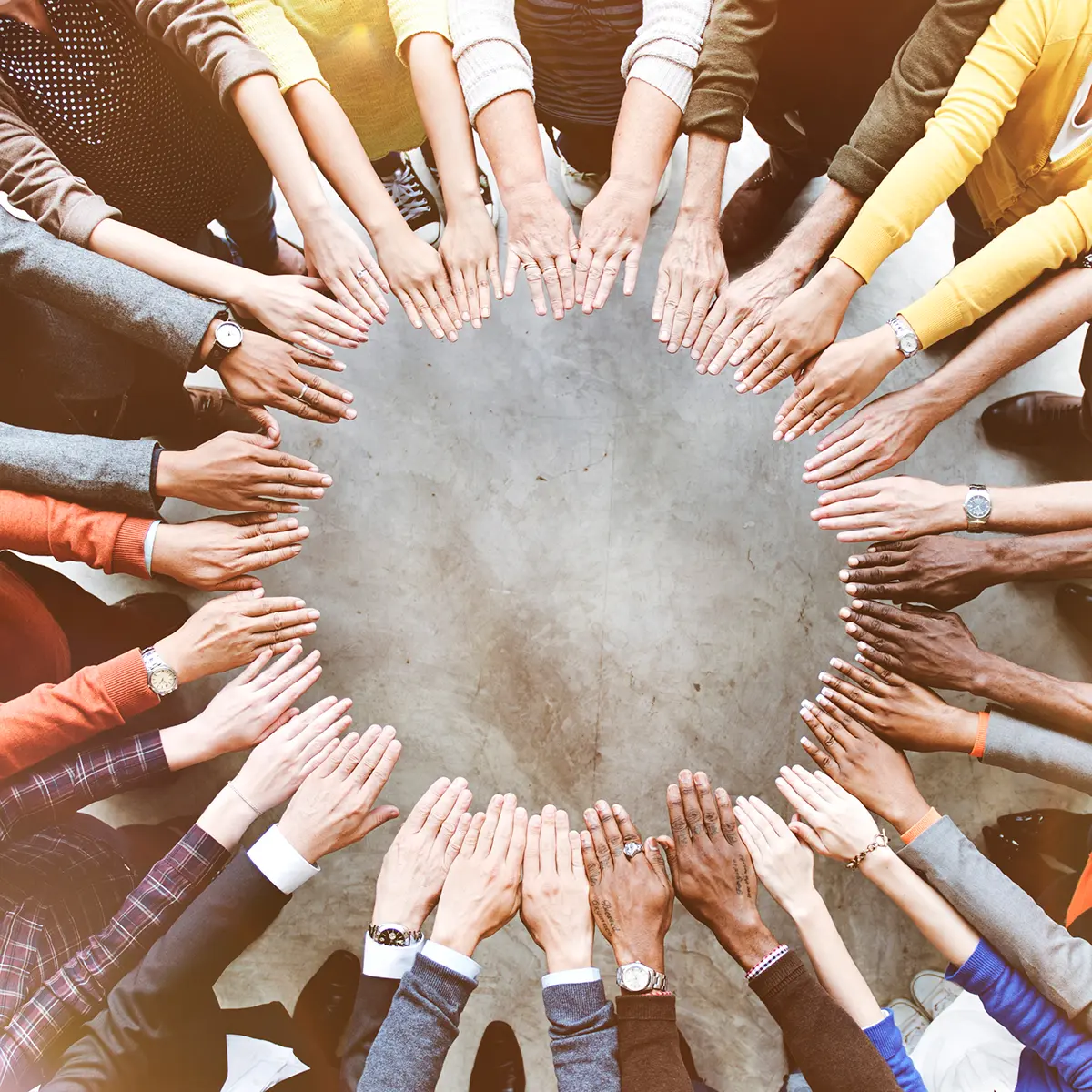 Aerial view of a diverse group placing their hands together in a circle, symbolising teamwork and unity