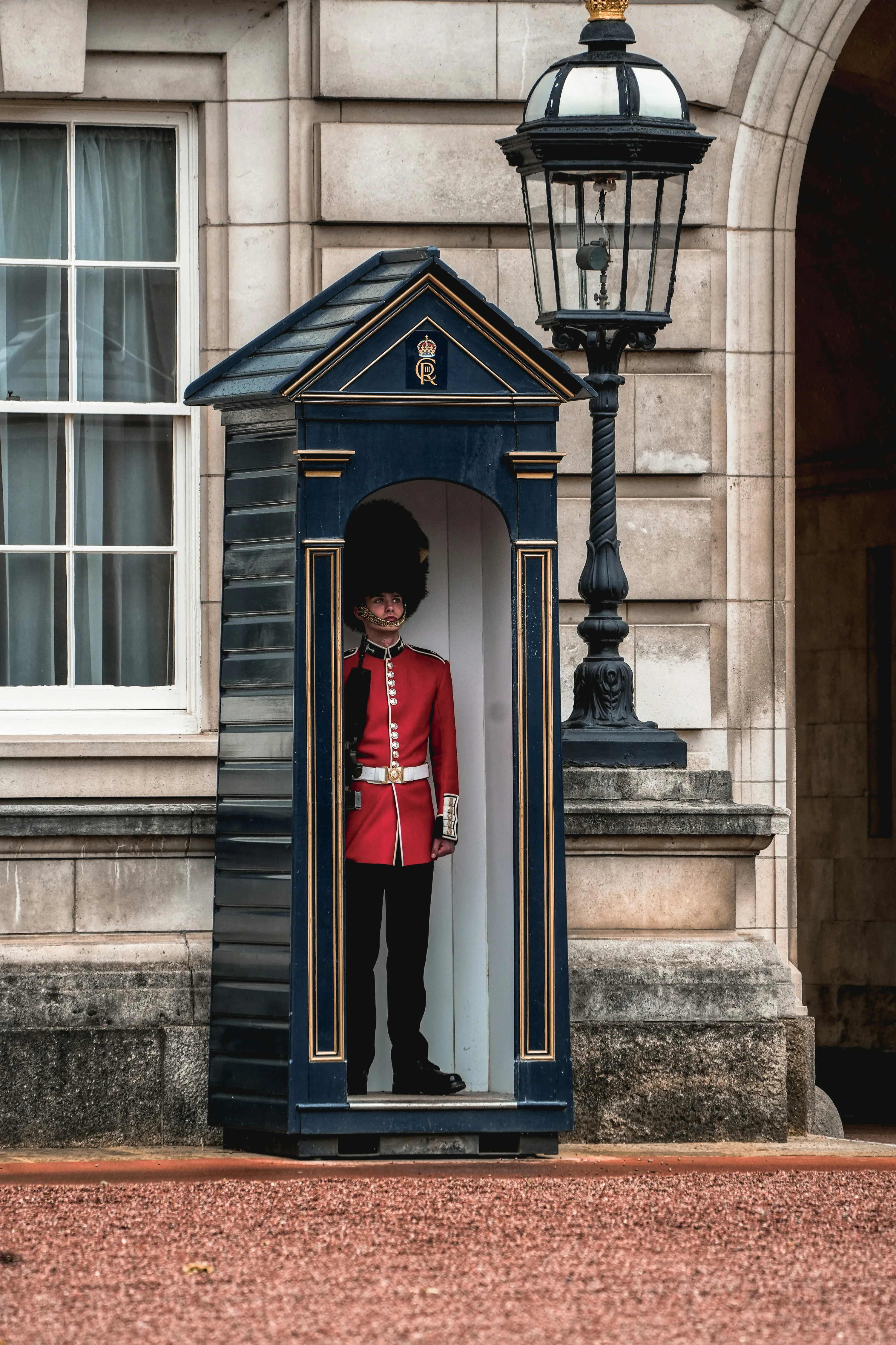 A royal guard at his post, clothed in signature red jacket, in front of Buckingham Palace.