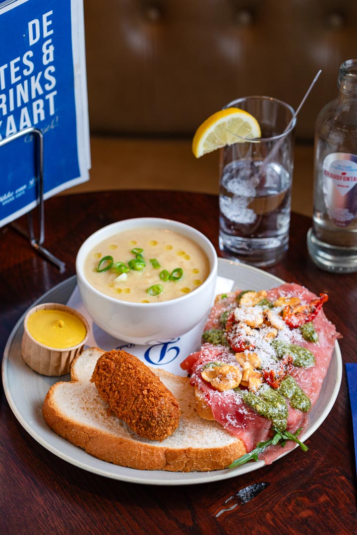 Een lunchgerecht met onder andere een brood waar een kroket op licht, een soepje en zalm