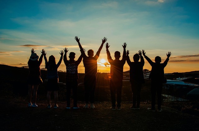 Silhouetted group raising hands against sunset sky.