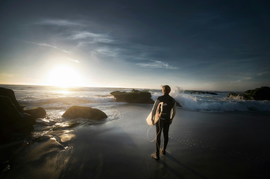 A person holding a surfboard looking at the sunrise