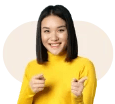 A young woman in a yellow sweater smiles and gestures with her hands in front of a light background.